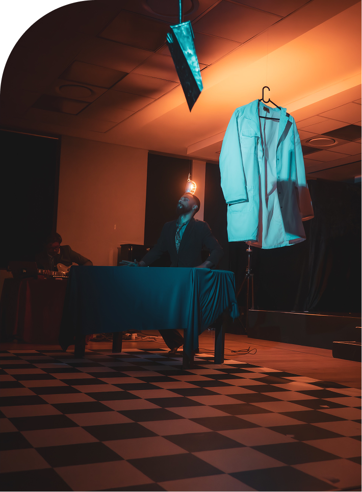 A man sits at a table, with a coat hanging from the ceiling above him.